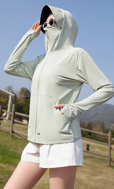 Woman wearing a green sun protection jacket with a hood, standing outdoors.