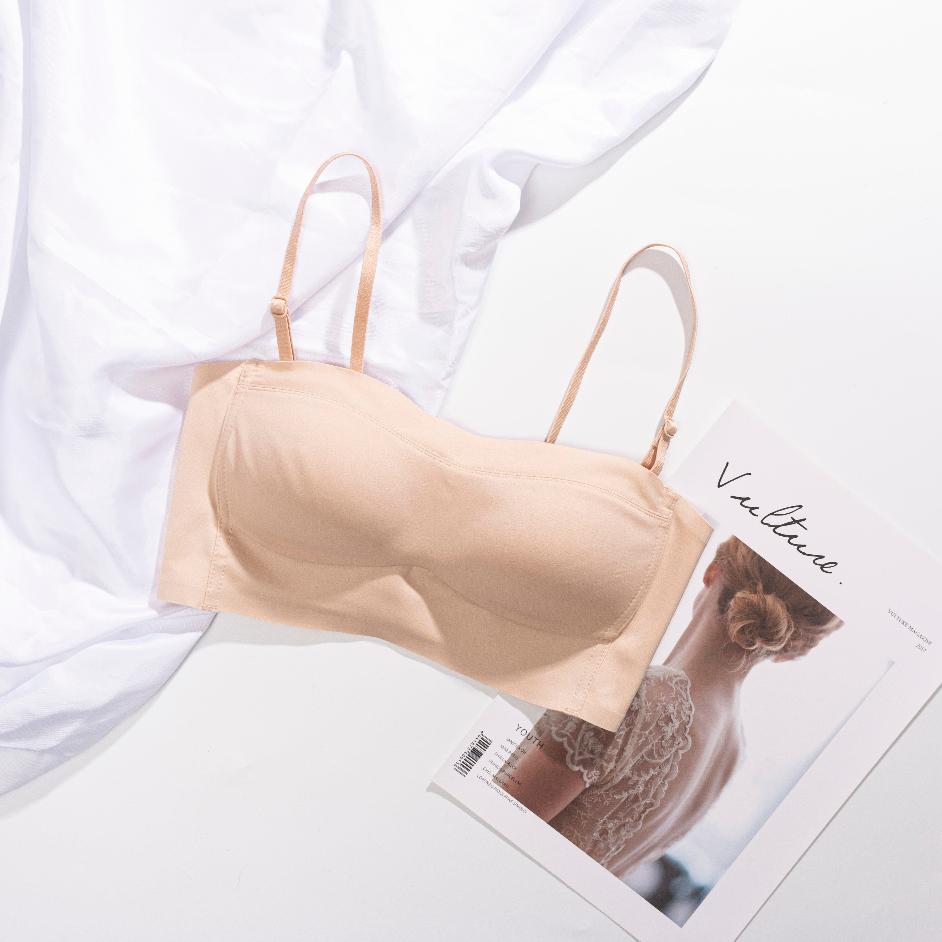 Front view of a beige strapless bra displayed on a flat surface, with removable straps beside it.